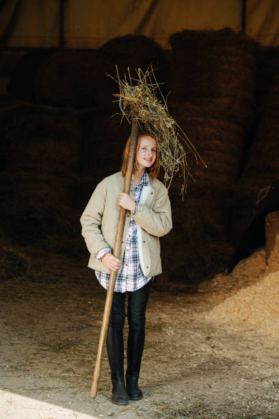 istock Funny little ginger girl standing inside a barn with pitchfork in hands 1283481366