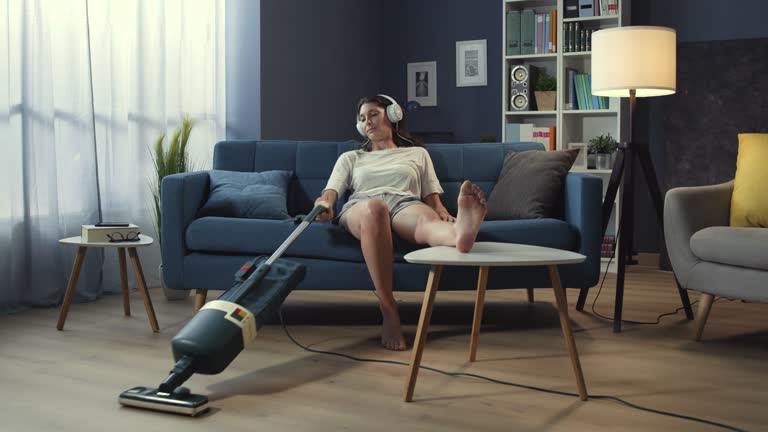 Lazy woman sitting on the sofa and vacuuming the floor