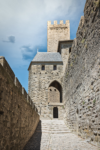 Carcasonne, France - July, 23rd 2018: Cobblestone street along the medieval fortified city wall of Carcasonne under blue sunny sky. Medieval stone wall surrounding the old town. Carcasonne, Languedoc Rousillon, South France, France, Europe.