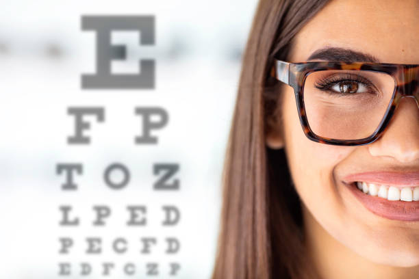 close up of young woman wearing eyeglasses with eyechart in the background. - sensory perception eyeball human eye eyesight imagens e fotografias de stock