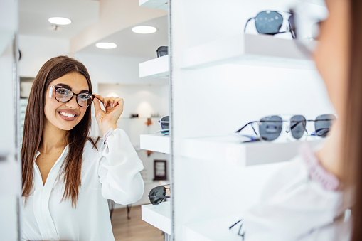 Shot of a young woman trying on a new pair of glasses at an optometris. Deciding which pair fits best. Beautiful woman with optician trying eyeglasses