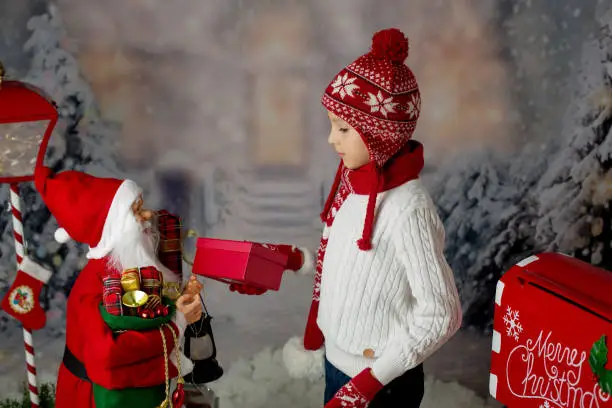 Photo of Little child, boy, sending letter to santa in christmas mailbox, christmas decoration around him