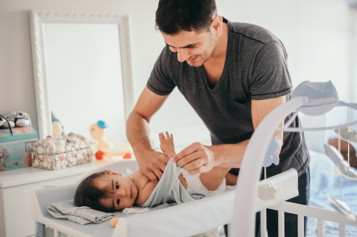 Family time. Handsome father changing diaper to his baby boy at home