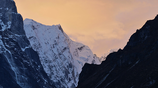 Craggy mountain range with majestic ice-capped mountains in the Himalayas with slightly orange colored cloudy sky at sunset near village Thame, Khumbu region, Nepal.