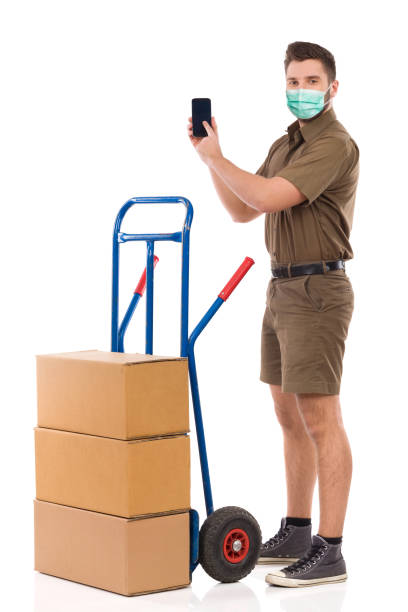 istock Messenger Is Standing Close To A Push Cart, Holding Smartphone And Pointing At It 1283496263