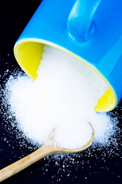 istock Blue cup pouring sugar and wooden spoon - black background. 1283496313