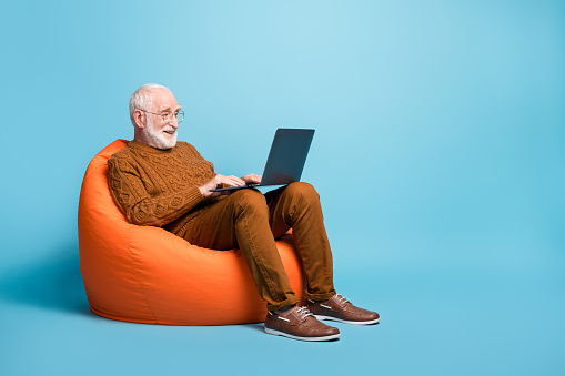 Retrato de su él agradable atractivo atractivo barbudo hombre de pelo gris sentado en la silla de la bolsa usando portátil escribiendo carta de correo electrónico navegando web wi-fi aislado sobre el fondo de color azul pastel photo