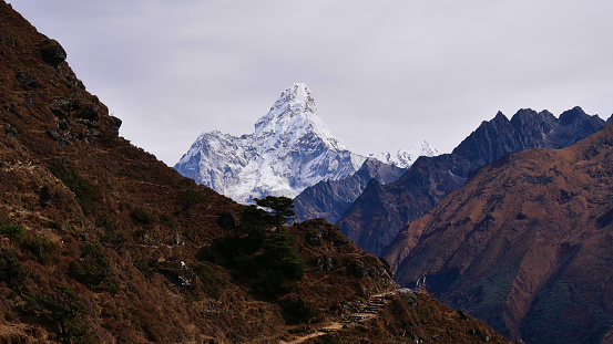 Stunning view of majestic ice-capped mountain Ama Dablam (peak 6,814 m) with footpath in foreground on Everest Base Camp Trek near Namche Bazar, Khumbu, Himalayas, Nepal on cloudy day.