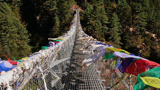 Colorful Buddhist prayer flags peacefully flying in the wind on popular Hillary Suspension Bridge on the way up to Namche Bazar, Himalayas, Nepal on Everest Base Camp Trek.