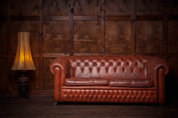 beautiful leather sofa chester brown. in the interior of the loft of dark color, with a wooden wall in the background. there are two insides - a sofa and a floor lamp - armchair sofa leather brown imagens e fotografias de stock