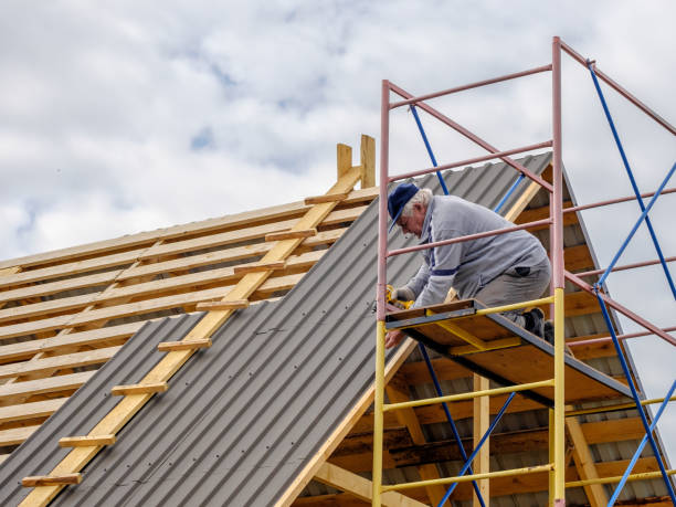 istock Senior gray-haired Construction man using a screwdriver, fastens a roofing sheet to wooden rafters on the roof of a country house under construction. 1283498555
