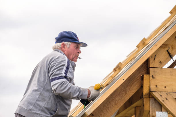 istock Senior gray-haired Construction man using a screwdriver, fastens a roofing sheet to wooden rafters on the roof of a country house under construction. 1283498650