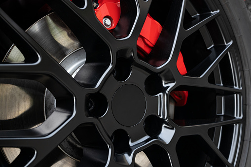 Black Wheel rim and red brake caliper of a sport car. Close up
