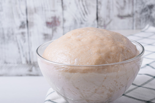 Yeast dough in a glass bowl ready to be formed into bakery products against white background