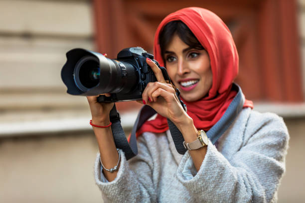 Arab Woman Photographer in a scarf taking picture using Camera Arab Female photographer takes a photo with a digital camera. A Mature Muslim Woman photographing you with a camera. Photographer with a lens in his hand on a city street. muslim photographer stock pictures, royalty-free photos & images