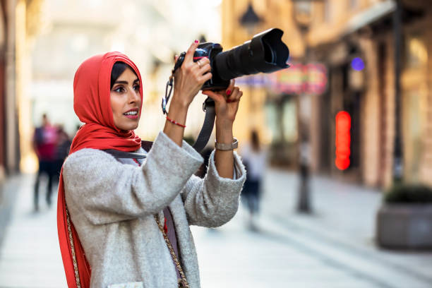 Muslim Woman with camera on the street. Arab Female photographer takes a photo with a digital camera. A Mature Muslim Woman photographing you with a camera. Photographer with a lens in his hand on a city street. muslim photographer stock pictures, royalty-free photos & images