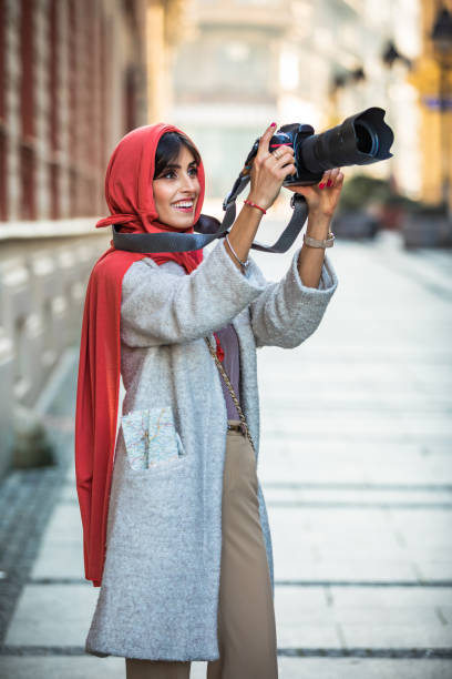 Muslim Woman with camera on the street. Arab Female photographer takes a photo with a digital camera. A Mature Muslim Woman photographing you with a camera. Photographer with a lens in his hand on a city street. muslim photographer stock pictures, royalty-free photos & images