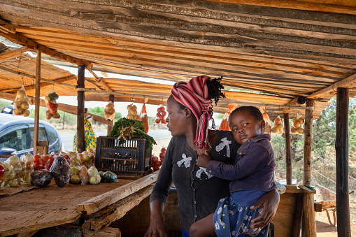 african woman holding her child,  street vendor with entrepreneurial spirit, selling vegetables on a wooden table