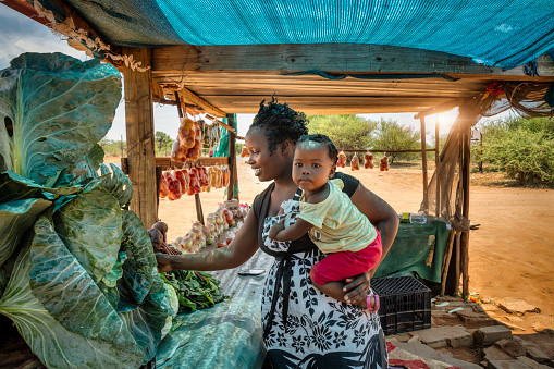 african street vendor, mother holding her child between the bags of tomatoes and cabbage