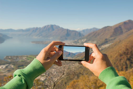 Woman Taking a Photo of the Mountain and Alpine lake Maggiore with Mobile Phone in Ticino, Switzerland.