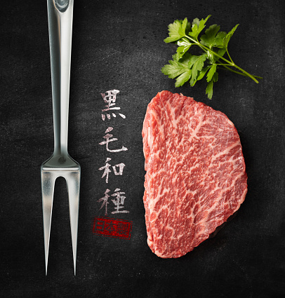 Kobe beef filet with fork and japanese text on black background\nIn Japan, the word \