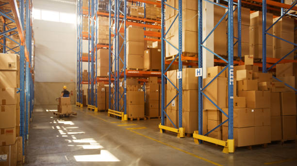 istock Worker Moves Cardboard Boxes using Manual Pallet Truck, Walking between Rows of Shelves with Goods in Retail Warehouse. People Work in Product Distribution Logistics Center. Side View 1283514214