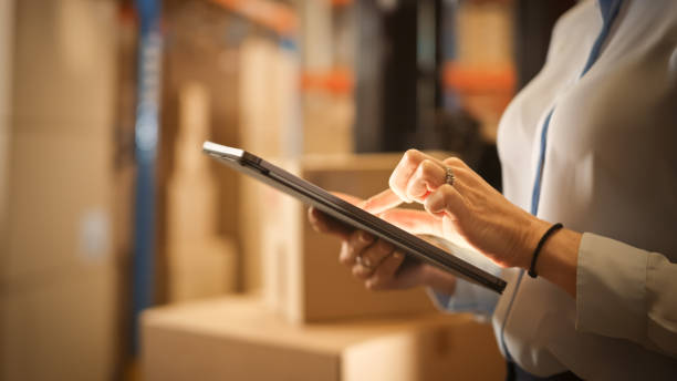 in warehouse manager uses digital tablet does inventory, using touch screen gestures, checking package delivery. distribution center with shelves with cardboard boxes. focus on hands and device - logistical imagens e fotografias de stock