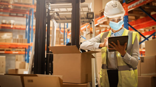 istock Female Warehouse Inventory Manager Wearing Face Mask for Safety, Using Digital Tablet Computer, Checking Cardboard Boxes. Delivery Distribution Center with Goods, Products Ready for Shipment 1283514252