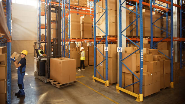 Retail Warehouse full of Shelves with Goods in Cardboard Boxes, Workers Scan and Sort Packages, Move Inventory with Pallet Trucks and Forklifts. Product Distribution Delivery Center. almacén al por menor lleno de estantes con mercancías en cajas de cartón, paquetes de escaneo y clasificación de trabajadores, inventario de movimiento con camiones de palés y carretillas elevadoras. centro de entrega de distribución de productos.