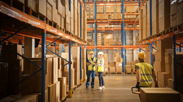 Retail Warehouse full of Shelves with Goods in Cardboard Boxes, Male and Female Managers Use Digital Tablet, Talk about Product Delivery. In Background Forklift Working in Logistics Storehouse Retail Warehouse full of Shelves with Goods in Cardboard Boxes, Male and Female Managers Use Digital Tablet, Talk about Product Delivery. In Background Forklift Working in Logistics Storehouse logistical stock pictures, royalty-free photos & images