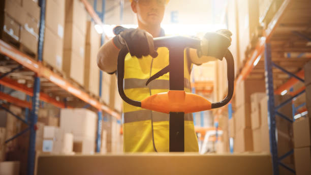 Worker Moves Cardboard Boxes using Hand Pallet Truck, Walking between Rows of Shelves with Goods in Retail Warehouse. People Work in Product Distribution Logistics Center. Point of View Shot Worker Moves Cardboard Boxes using Hand Pallet Truck, Walking between Rows of Shelves with Goods in Retail Warehouse. People Work in Product Distribution Logistics Center. Point of View Shot logistical stock pictures, royalty-free photos & images