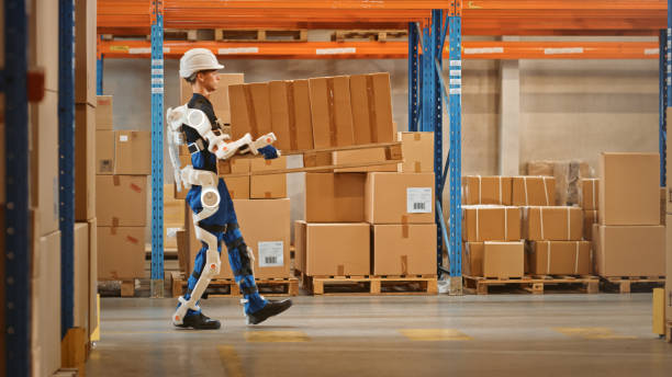 istock High-Tech Futuristic Warehouse: Manager Scans Packages for Inventory, Delivery in the Background Worker Wearing Advanced Full Body Powered exoskeleton, Walks with Heavy Pallet full of Cardboard Boxes 1283514333