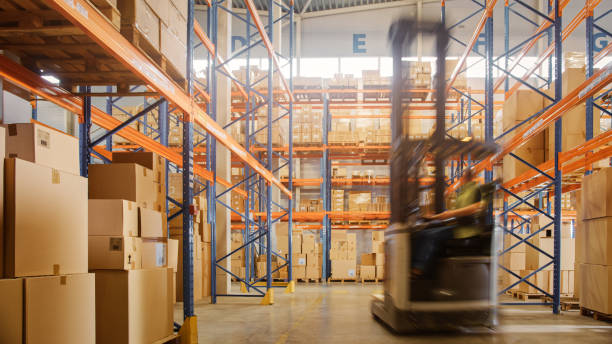 In Warehouse Shot of Blurred Forklift Driving with Pallets Moving Cardboard Boxes with Products from Shelves. Logistics Distribution Center with Products Ready for Global Shipment, Customer Delivery. In Warehouse Shot of Blurred Forklift Driving with Pallets Moving Cardboard Boxes with Products from Shelves. Logistics Distribution Center with Products Ready for Global Shipment, Customer Delivery. logistical stock pictures, royalty-free photos & images