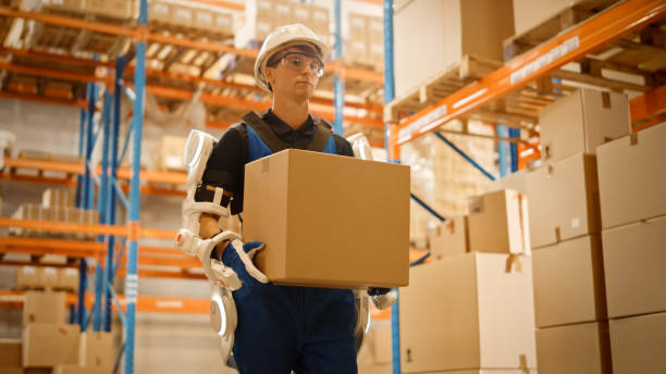 istock High-Tech Futuristic Warehouse: Worker Wearing Advanced Full Body Powered exoskeleton, Walks with Heavy Cardboard Box. Exosuit amplifies Human strength. Low Angle Portrait Shot 1283514403