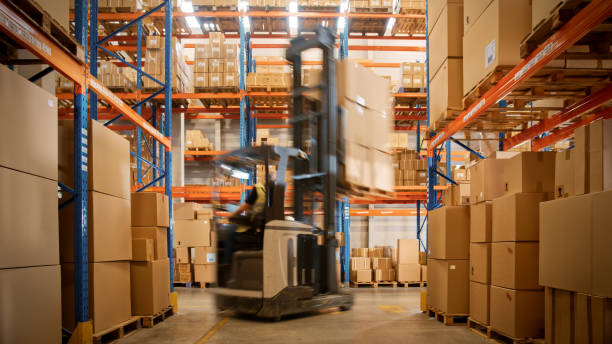 In Warehouse Shot of Blurred Forklift Driving with Pallets Moving Cardboard Boxes with Products from Shelves. Logistics Distribution Center with Products Ready for Global Shipment, Customer Delivery. In Warehouse Shot of Blurred Forklift Driving with Pallets Moving Cardboard Boxes with Products from Shelves. Logistics Distribution Center with Products Ready for Global Shipment, Customer Delivery. logistical stock pictures, royalty-free photos & images