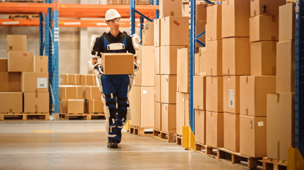 istock High-Tech Futuristic Warehouse: Worker Wearing Advanced Full Body Powered exoskeleton, Walks with Heavy Cardboard Box. Exosuit amplifies Human Performance, strength, Eliminates Work Related Injuries 1283514499