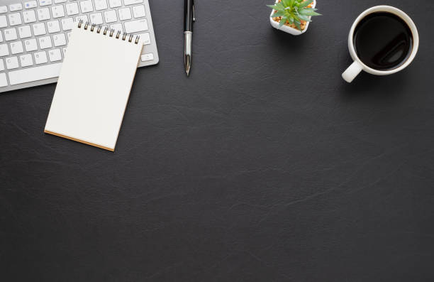 istock Black office desk table with keyboard, notebook and coffee cup with equipment other office supplies. Business and finance concept. Workplace, Flat lay with blank copy space. Top view 1283514572