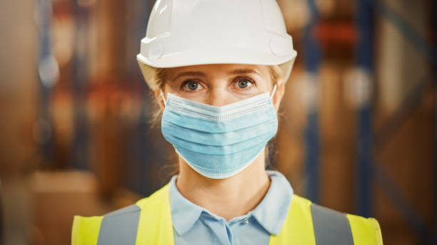 portrait of the successful female warehouse inventory manager wearing face mask for safety. in background rows of shelves with merchandise, goods, products packed in cardboard boxes ready for shipment - logistical imagens e fotografias de stock