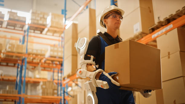 istock High-Tech Futuristic Warehouse: Worker Wearing Advanced Full Body Powered exoskeleton, Walks with Heavy Cardboard Box. Exosuit amplifies Human strength. Low Angle Portrait Shot 1283514589