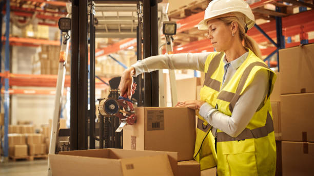 female warehouse inventory manager finishes packing cardboard box closing it and sealing with tape dispenser sealer. delivery distribution center with goods, products ready for shipment - logistical imagens e fotografias de stock