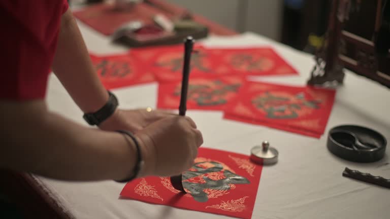 hand of asian chinese male practising chinese caligraphy for coming chinese new year celebration home decoration purpose with prosperity and good wording by writing it on a red piece of paper