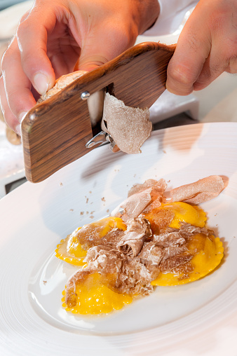 hands of the waiter serve Alba white truffle sliced on Italian egg pasta ravioli