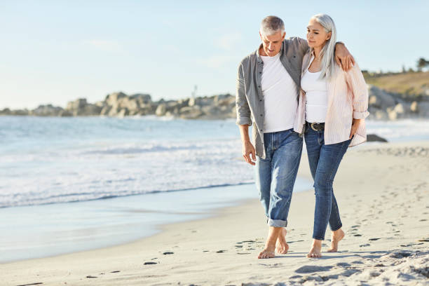 Romantic couple in casuals walking at beach Romantic couple talking while walking at beach. Mature man and woman are enjoying during vacation. They are in casuals. 50 59 years stock pictures, royalty-free photos & images