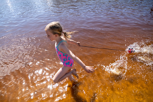 A young blond girl running through the water at the beach. She is having fun on her summer vacation.