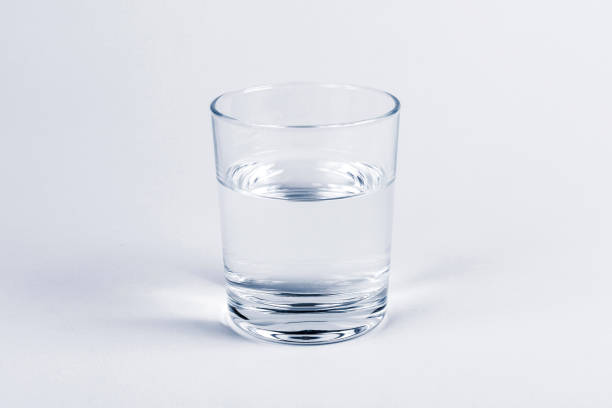 istock One simple half full half empty glass of fresh crystal clear clean drinking water, solo object isolated on light blue background. Hydration and health symbol, minimal, minimalistic concept, closeup 1283524975