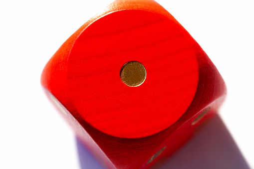 Simple red game dice showing one. Number 1 on a big wooden playing dice on white background, macro, extreme closeup. Low score, lost game, bad luck and misfortune in gambling, gaming abstract concept