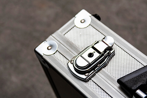 Silver metal suitcase, box, crate or simple case with a handle for equipment, valuables or money secure transport closeup. Safe storage abstract concept. Focus on the briefcase lock clip mechanism