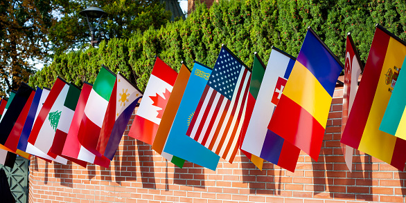 Row of many different flags hanging from a brick wall during the day. Representing of countries Multi cultural event, mix of culture patriotic symbols, many nationalities, nations abstract concept.