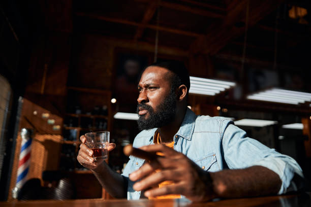 handsome afro american man smoking cigar and drinking whisky - cigar whisky bar cognac imagens e fotografias de stock