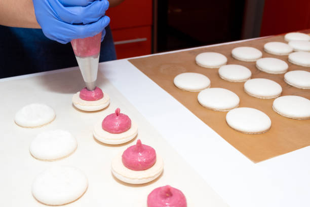 applying the filling from the pastry bag to the macaroon. the process of making dessert. - fragility organization chef cake imagens e fotografias de stock